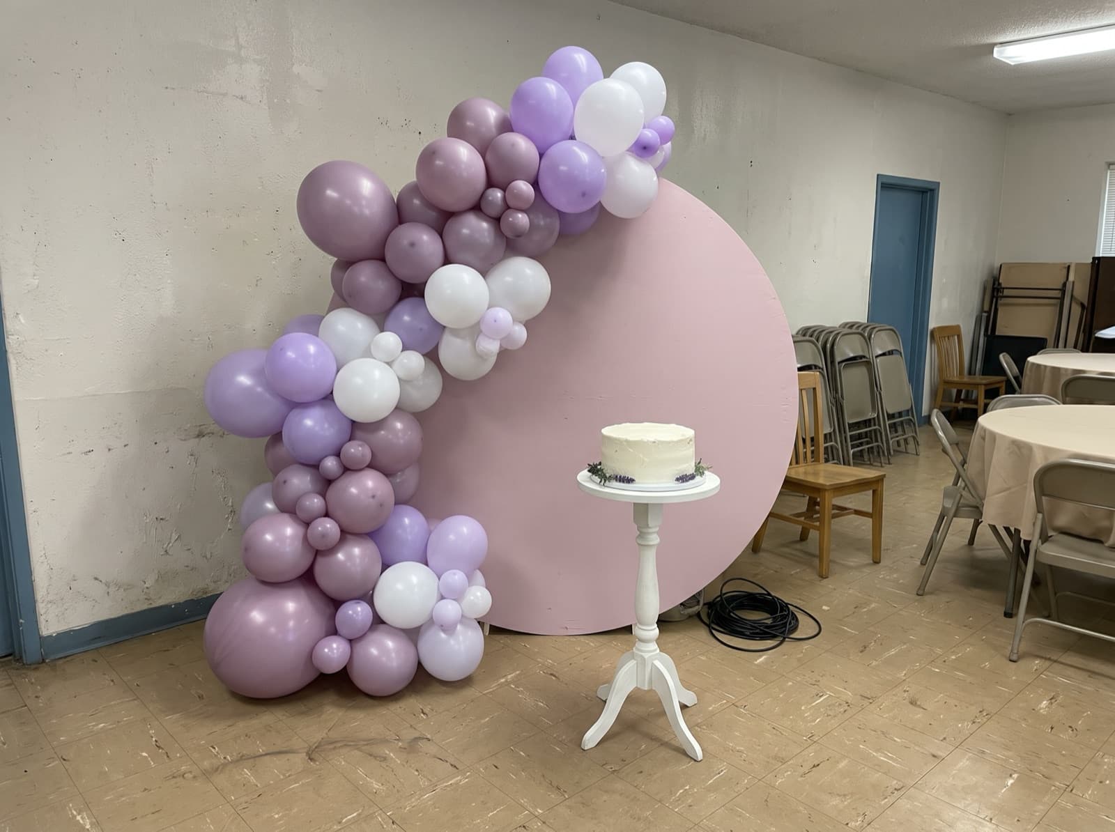 Round balloon backdrop with a lavender and white organic garland and a cake stand at an Atlanta birthday party